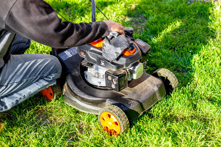 Caring for a petrol lawn mower after mowing the grass. A man wipes the body of the mower with a rag.の写真素材