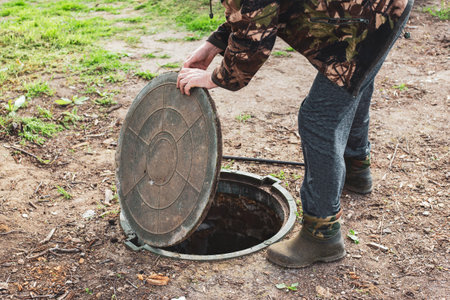 A man opened the septic tank hatch to check the sewer drain level. Septic tanks in a country house.