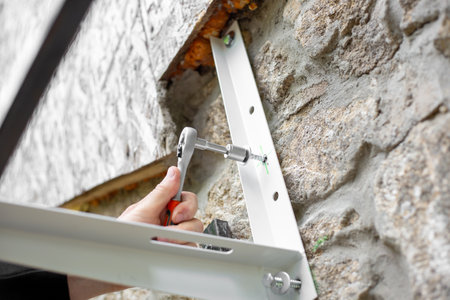 A man uses a ratchet wrench with a socket to screw a screw into a metal bracket to install on the...