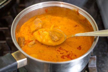 Making massaman curry. Stirring the dish with a spoon in a saucepan on the stove.の写真素材