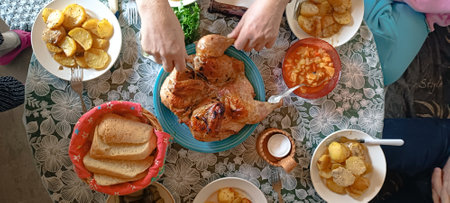Male hands cutting baked chicken with a knife, which lies on a plate in the middle of a served...