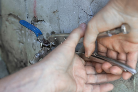 A man uses an adjustable wrench to tighten a metal faucet on a concrete wall.の写真素材