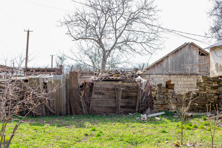 Scene of desolation with crumbling building and overgrown foliage in rural area. Old house and barns in village.の写真素材