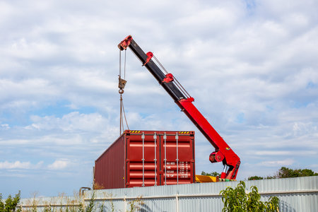 A red crane lifts a red cargo container, preparing for transportation.