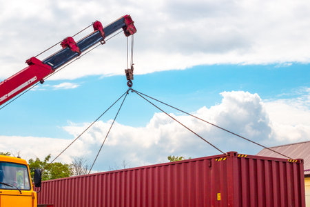 A brightly colored container is lowered into place by a red and yellow crane.