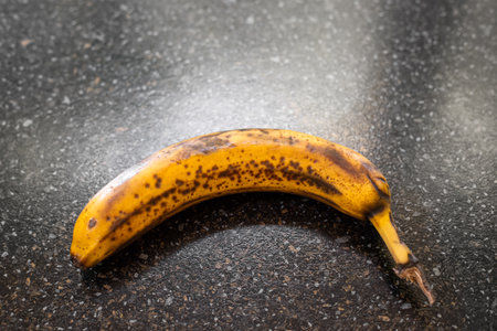 An overripe banana with brown spots lies on a dark countertop, highlighting the natural aging process.の写真素材