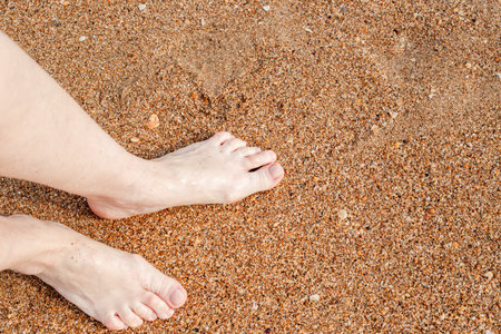 Bare feet standing on a sandy beach capturing a simple moment of relaxation and unity with nature,...