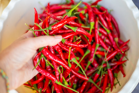 Hand takes handful of chili peppers from bowl. Spice harvest.