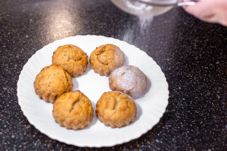 A baker dusts homemade muffins with powdered sugar, adding a subtle sweetness and decorative touch.の写真素材