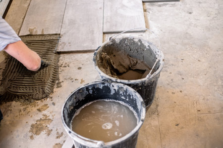Preparing tile adhesive in buckets during a flooring renovation project using large format tiles....