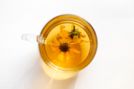 Top view of clear glass mug filled with golden tea and yellow flowers on white surface.の写真素材