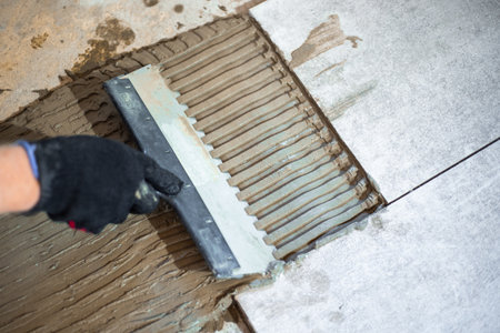 Applying tile adhesive with a notched trowel to the floor before laying large-format tilesの写真素材