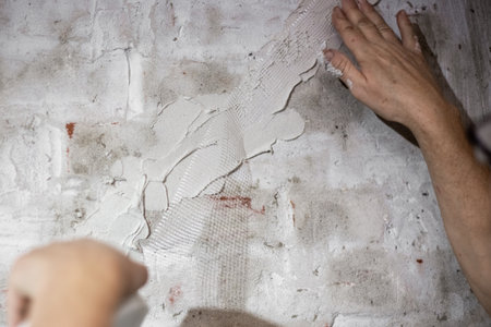 Close-up of worker smoothing mesh tape on freshly plastered brick wall to repair cracks.の写真素材