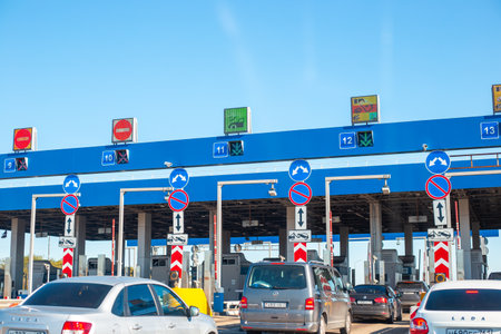 Cars patiently wait for them to turn at a toll plaza with clear lane markings and digital displays....
