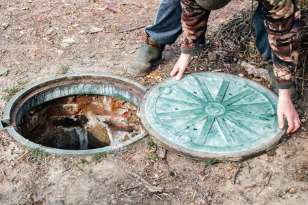 A man about to close a septic tank manhole cover after checking the sewer level.の写真素材