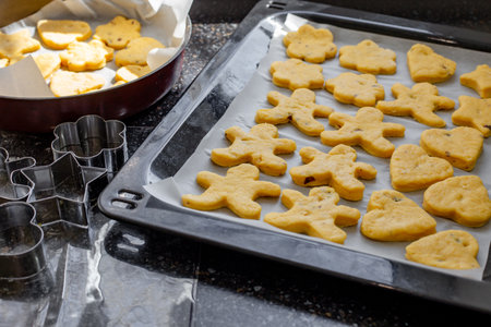 Homemade cookies of various shapes are arranged on baking sheets, ready to bake in the warm and cozy...
