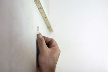 A hand holds a small metal bracket on a light-colored surface, preparing for installation.