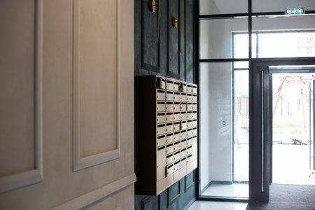 Modern wall-mounted mailboxes are located in the lobby of an apartment building next to the glass exit door.の写真素材