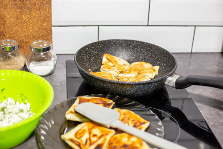Savory lavash pastries with cottage cheese are cooked in a frying pan and cooled on a plate, with a bowl of cheese and herb filling nearby.の写真素材