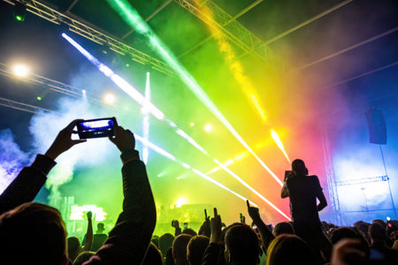 A man films a concert performance on his phone in a nightclub, capturing the energy of the stage and the crowd.の素材