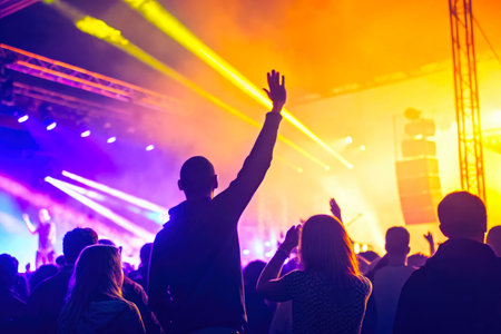 Silhouettes of people enjoying a concert with bright stage lights and laser beams.の素材