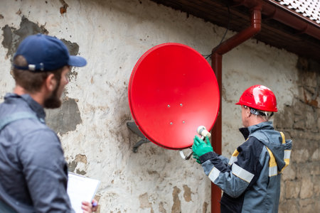 Two workers in overalls are setting up a satellite dish mounted on the wall of an old village house.の写真素材