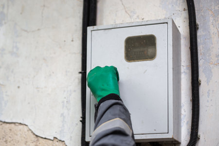 An electrician opens the door of a metal cabinet containing an electricity meter on the wall of an...