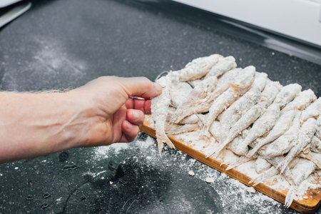A man prepares red mullet by coating it in flour and placing it on a cutting board for frying.の写真素材