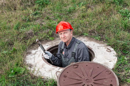 A plumber peers out from an open water well in a rural area. Plumbing repair and maintenance.
