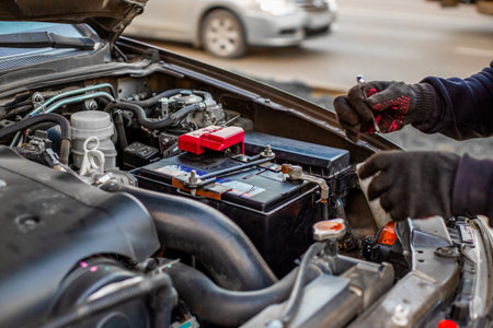 A man wearing gloves secures a car battery terminal after installing it under the hood. Replacing a...