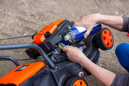 Man pouring engine oil into a lawnmower outdoors. garden equipment maintenance, technical service,...