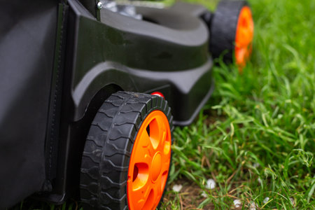 Close up of the orange wheels of a black lawn mower on fresh green grass. garden machinery, lawn care, outdoor equipment.の写真素材