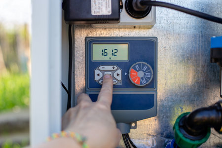 A hand operates a digital irrigation timer on a control panel in a garden. smart farming, automated...