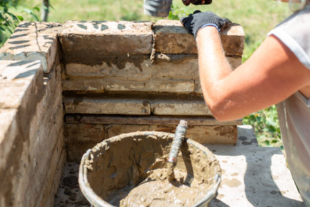 Close up of hands in gloves laying a brick for an outdoor oven. masonry work, building process,...