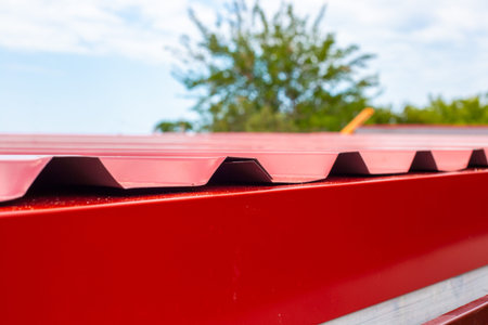 Close up of the edge of a red corrugated metal roof against a soft sky. industrial texture, metal...
