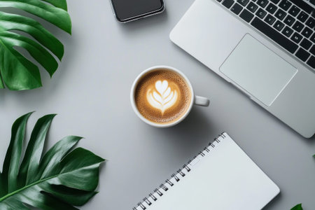 A top-down flat lay of a laptop, smartphone, coffee, and green leaves on a grey background. Aesthetic workspace, digital workflow, creative desk.の素材