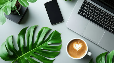 A top-down flat lay of a laptop, smartphone, coffee with heart latte art, and green leaves on a grey desk. Creative workspace, romantic drink, digital content.の素材