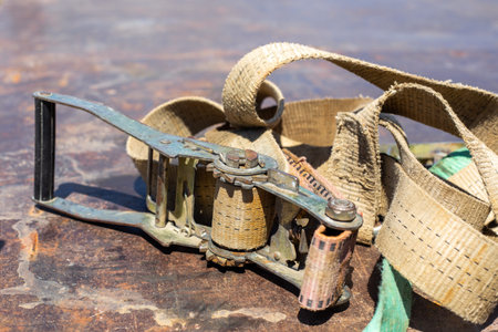 Close up of a metal ratchet mechanism with beige straps on a worn industrial surface. cargo...