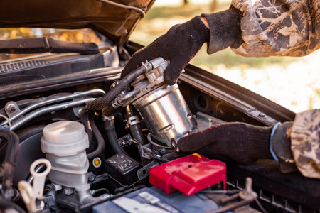 A mechanic in gloves removes a fuel filter from a car engine. car repair, auto service, maintenance workの写真素材