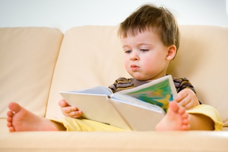 Little boy reading book on sofa の写真素材