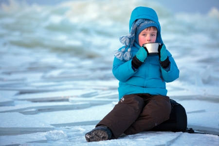 Portrait of cute little boy with metal thermos cup of hot tea in winter outdoorsの写真素材