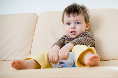 Little boy sitting on sofa with a book in handsの写真素材