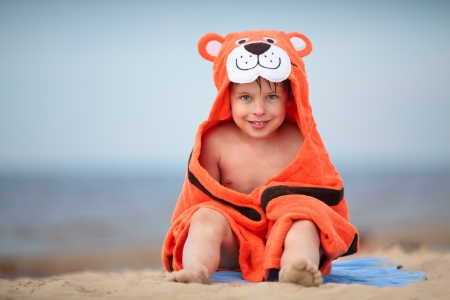 Cute little boy wearing tiger towel sitting at the beachの写真素材