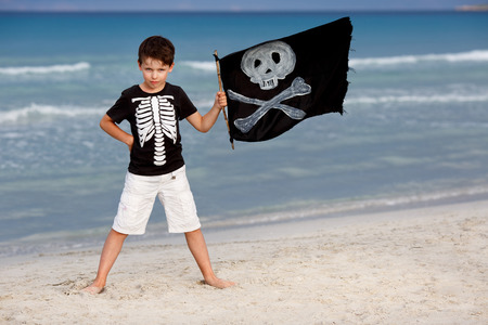 Cute boy dressed as pirate and holding a black flag on tropical beach の写真素材