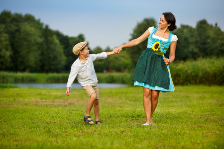 Attractive young woman in a dirndl with her son on meadowの写真素材