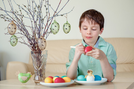 Cute little boy painting colorful Easter egg for hunt indoorsの写真素材