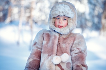 Portrait of little boy playing outdoors in forest on beautiful winter snowy day