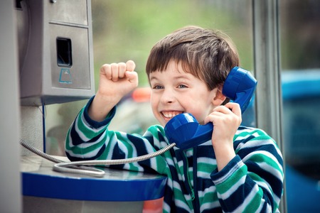 Cute little boy is calling home using the public payphoneの写真素材