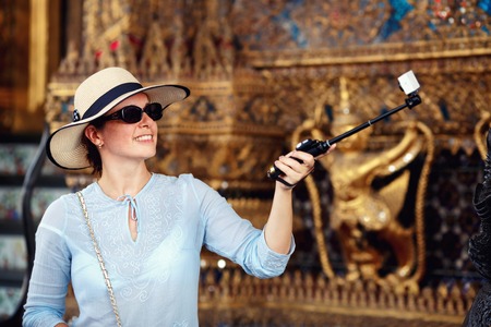 Young woman with hat and sunglasses making selfie with thai temple backgroundの写真素材