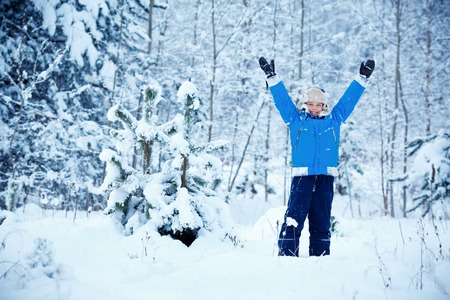 Cute little boy wearing warm clothes playing on winter forestの写真素材